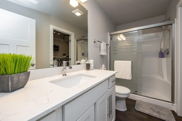 bathroom featuring toilet, wood finished floors, a spacious closet, vanity, and a shower stall