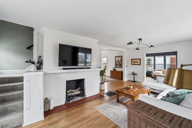 living room with light wood-style flooring, baseboards, stairs, ornamental molding, and a brick fireplace