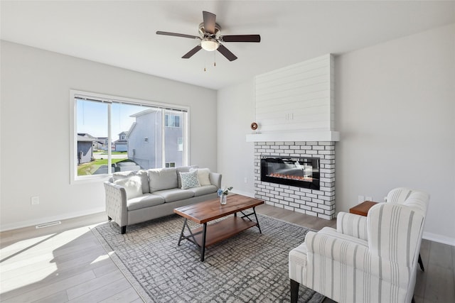 living room featuring a ceiling fan, a glass covered fireplace, baseboards, and wood finished floors