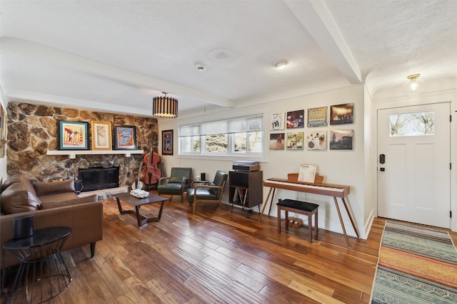 living area with a stone fireplace, beamed ceiling, a textured ceiling, and wood finished floors