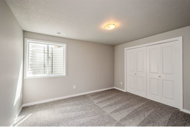 unfurnished bedroom featuring carpet, a closet, a textured ceiling, and baseboards