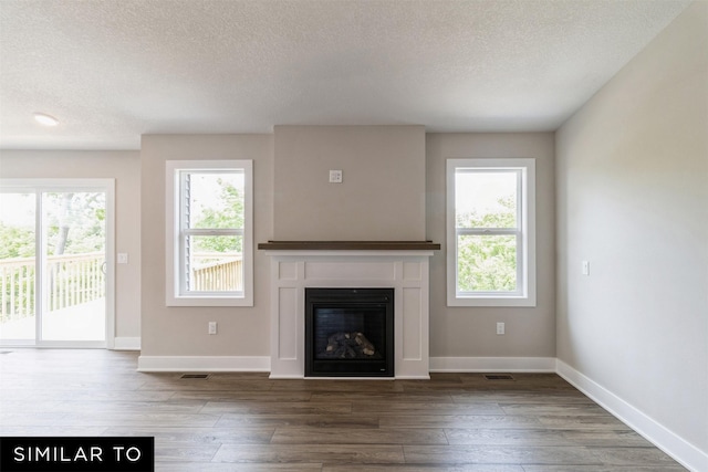 unfurnished living room featuring plenty of natural light, wood finished floors, and a glass covered fireplace