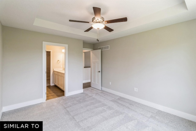 unfurnished bedroom featuring baseboards, visible vents, a raised ceiling, a ceiling fan, and light colored carpet