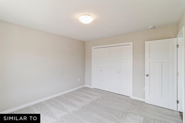 unfurnished bedroom with a closet, light colored carpet, a textured ceiling, and baseboards