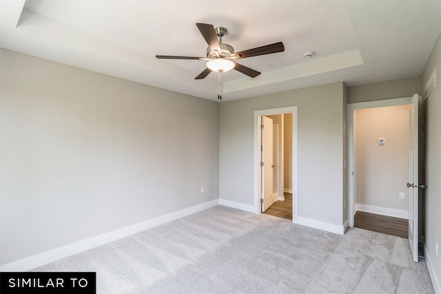 unfurnished bedroom with a ceiling fan, a raised ceiling, light colored carpet, and baseboards