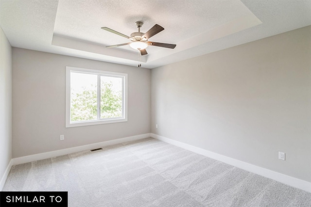 spare room with light carpet, a tray ceiling, visible vents, and a textured ceiling