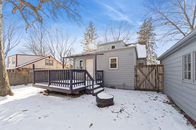 snow covered house with a gate, fence, and a deck