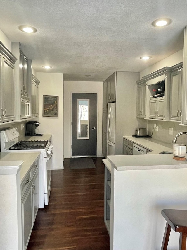 kitchen featuring dark wood-style flooring, light countertops, a sink, white appliances, and a peninsula