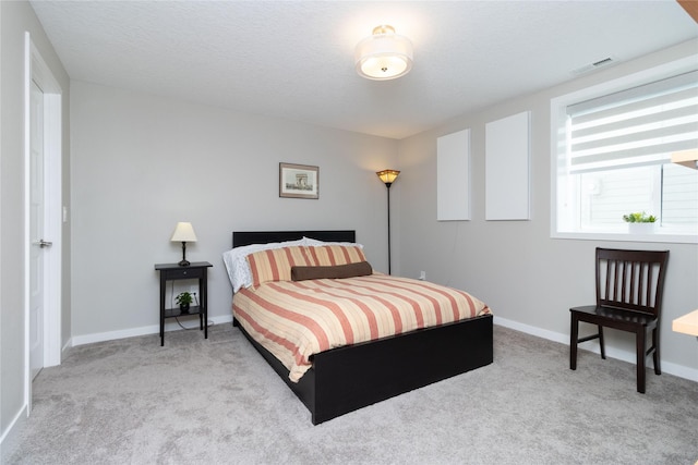 bedroom with light carpet, a textured ceiling, visible vents, and baseboards