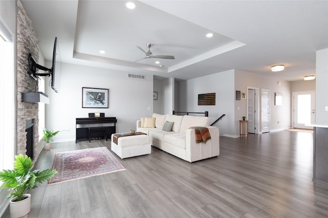 living room with a stone fireplace, a tray ceiling, wood finished floors, and visible vents