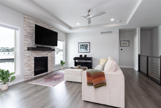 living area with visible vents, a raised ceiling, a wealth of natural light, and a stone fireplace