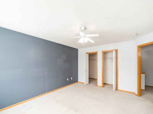 unfurnished bedroom with multiple closets, light carpet, baseboards, and a ceiling fan