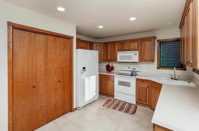 kitchen featuring white appliances, brown cabinets, light countertops, a sink, and recessed lighting