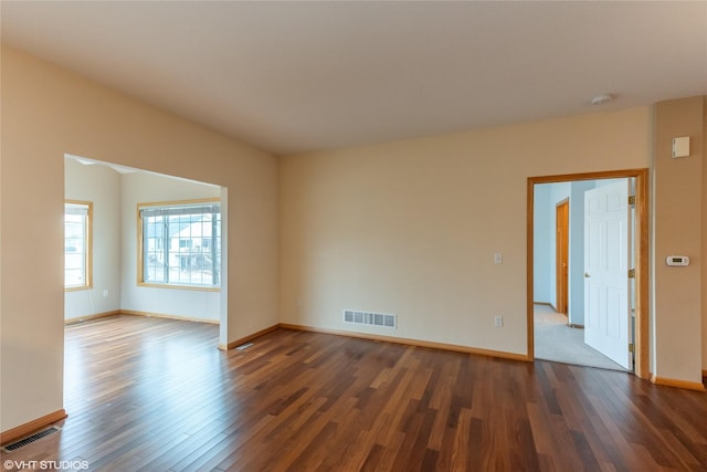 spare room with dark wood-style flooring, visible vents, and baseboards