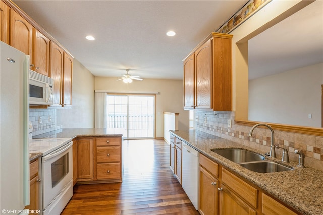 kitchen with white appliances, dark wood-type flooring, a peninsula, light stone countertops, and a sink