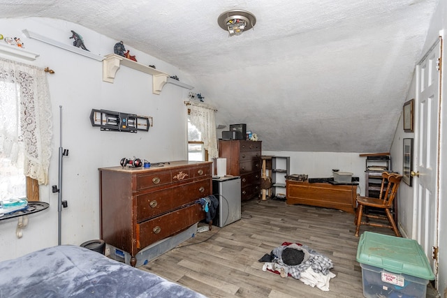 bedroom featuring light wood-type flooring, lofted ceiling, and a textured ceiling