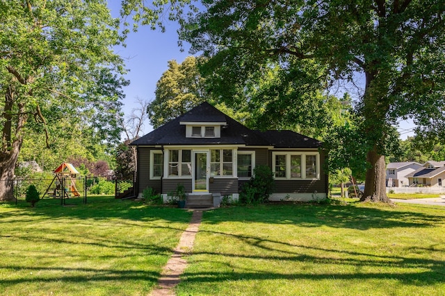 view of front of house featuring a playground, fence, and a front lawn