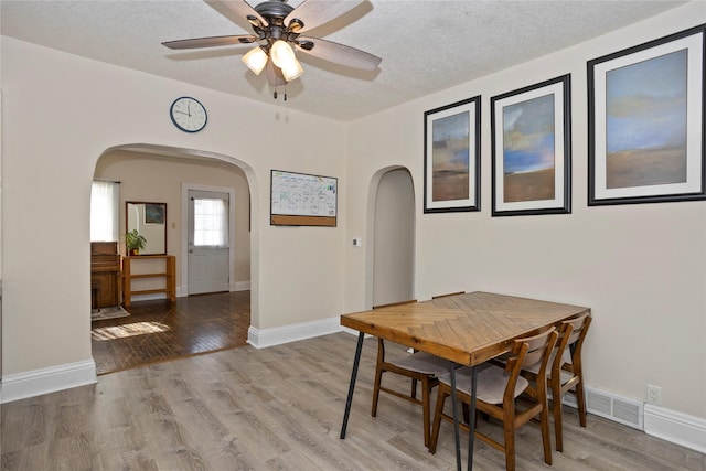 dining area with arched walkways, a textured ceiling, visible vents, and light wood-style floors