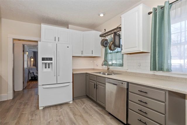 kitchen featuring white refrigerator with ice dispenser, light countertops, gray cabinetry, stainless steel dishwasher, and a sink