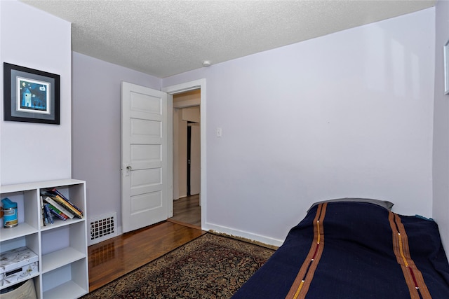 bedroom with dark wood-style flooring, visible vents, a textured ceiling, and baseboards