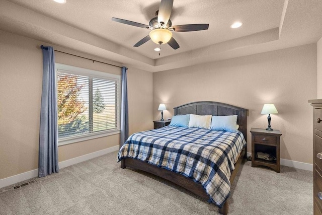 bedroom with a textured ceiling, a tray ceiling, light colored carpet, and baseboards