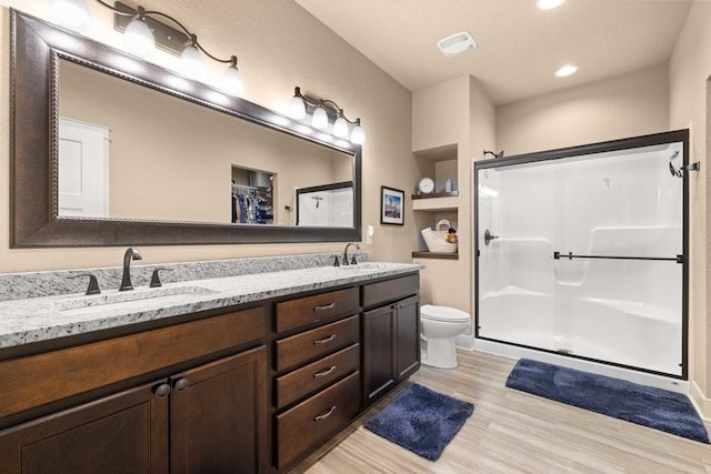 bathroom with double vanity, a stall shower, toilet, and a sink