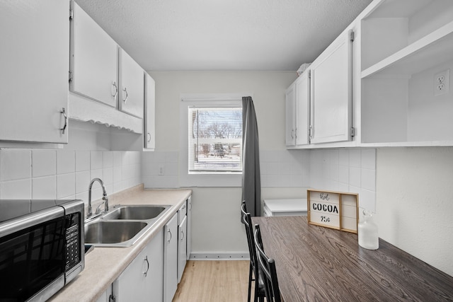 kitchen with light wood-style flooring, stainless steel microwave, light countertops, white cabinetry, and a sink