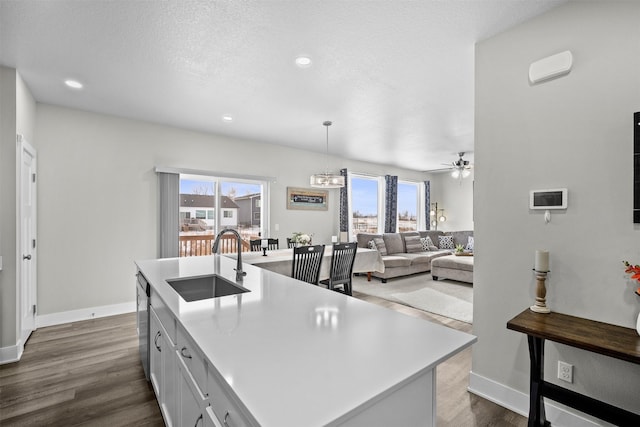 kitchen featuring a sink, white cabinetry, light countertops, hanging light fixtures, and a center island with sink