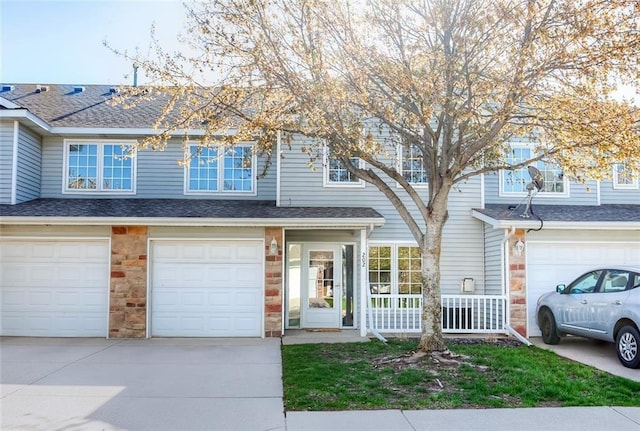 multi unit property with driveway, stone siding, an attached garage, and a shingled roof