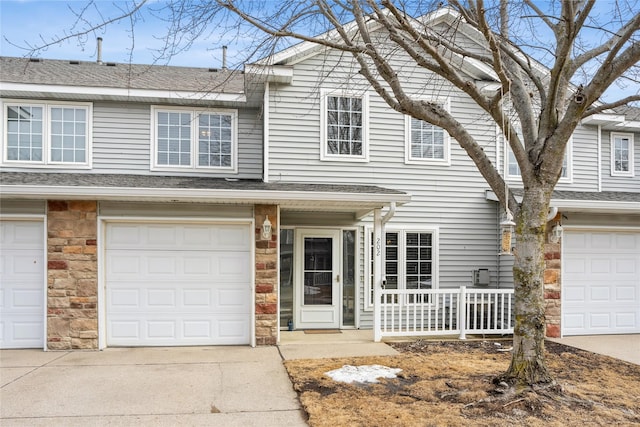 multi unit property featuring a garage, concrete driveway, roof with shingles, and stone siding