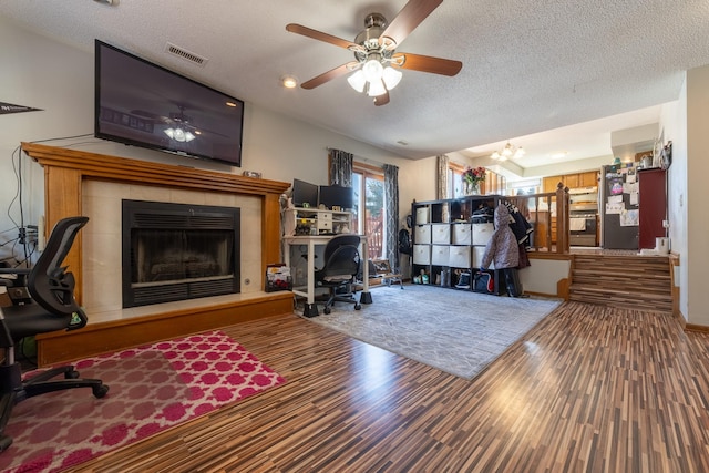 living area with a textured ceiling, a fireplace, wood finished floors, visible vents, and a ceiling fan