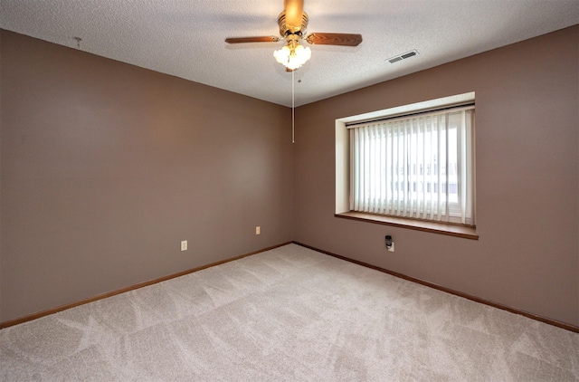 spare room with light carpet, baseboards, visible vents, a ceiling fan, and a textured ceiling