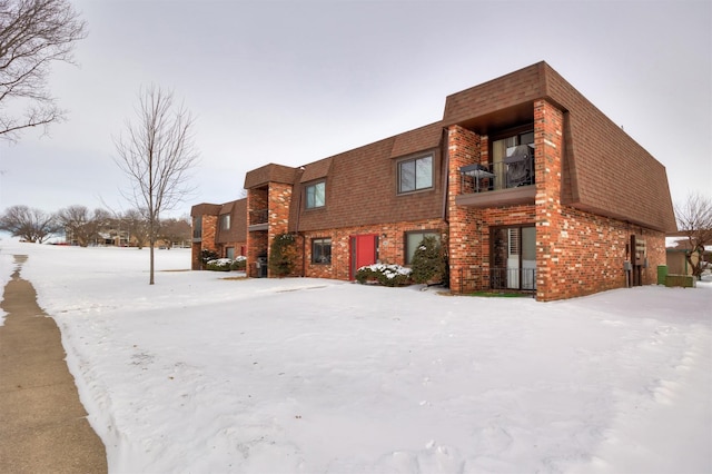 exterior space with a shingled roof, brick siding, and a balcony