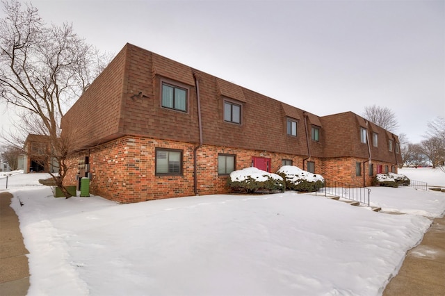 exterior space featuring a shingled roof, brick siding, and mansard roof