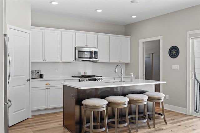 kitchen with stainless steel appliances, light countertops, a sink, and an island with sink