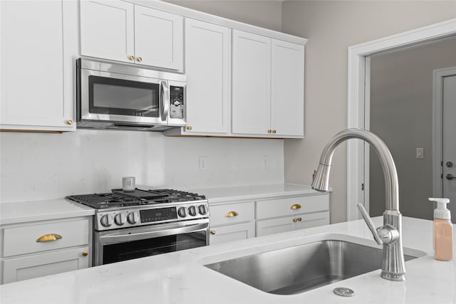 kitchen with light stone countertops, white cabinetry, stainless steel appliances, and a sink