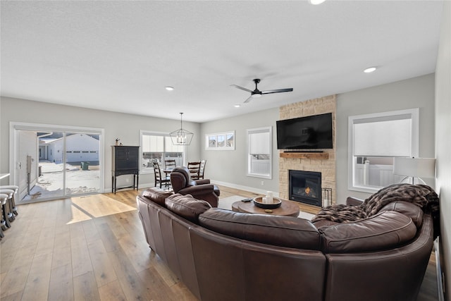 living room with a stone fireplace, recessed lighting, ceiling fan with notable chandelier, baseboards, and light wood finished floors