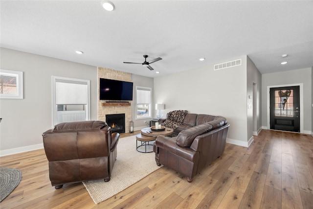 living area with a stone fireplace, light wood-style flooring, visible vents, and baseboards