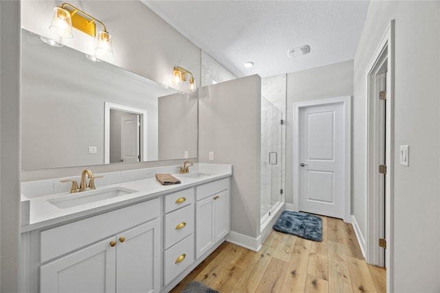 full bath with double vanity, a stall shower, a sink, and wood finished floors