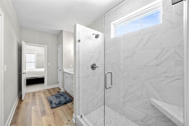 bathroom featuring a marble finish shower, connected bathroom, vanity, wood finished floors, and baseboards