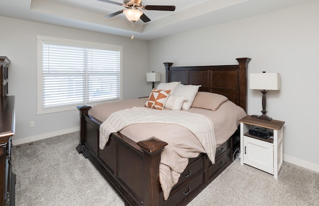 bedroom featuring baseboards, a tray ceiling, a ceiling fan, and light colored carpet