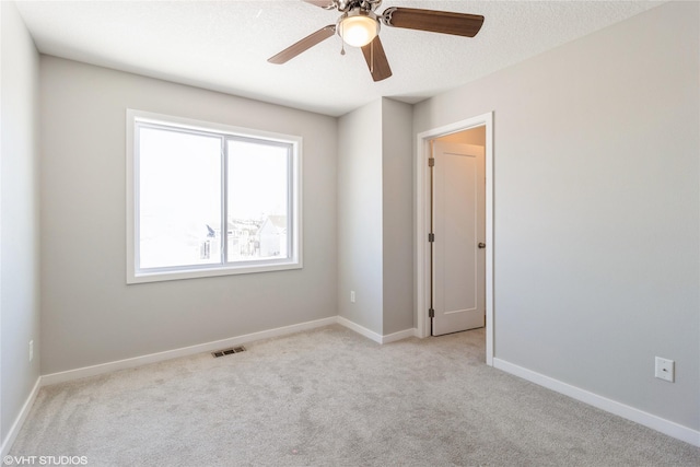 empty room featuring light colored carpet, visible vents, a ceiling fan, a textured ceiling, and baseboards