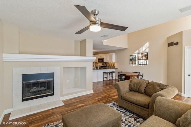 living room with dark wood-type flooring, a tile fireplace, ceiling fan, and a textured ceiling