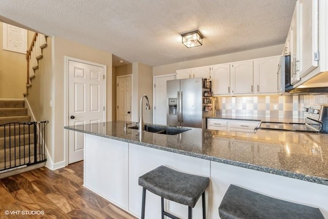 kitchen featuring dark stone counters, stainless steel refrigerator with ice dispenser, range, and white cabinetry