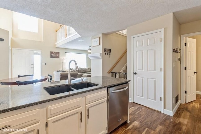 kitchen featuring dark wood finished floors, dark stone countertops, stainless steel dishwasher, a sink, and open floor plan
