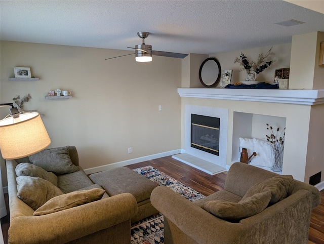 living area featuring a ceiling fan, wood finished floors, a textured ceiling, a tiled fireplace, and baseboards