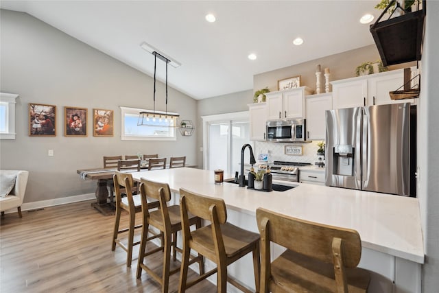 kitchen with appliances with stainless steel finishes, light countertops, white cabinetry, pendant lighting, and a sink