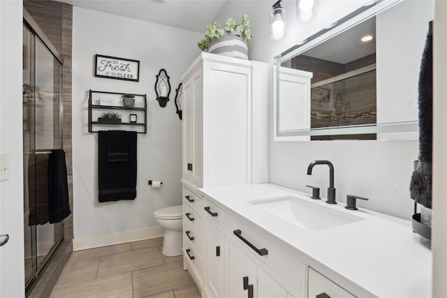 full bathroom with toilet, a stall shower, baseboards, and vanity