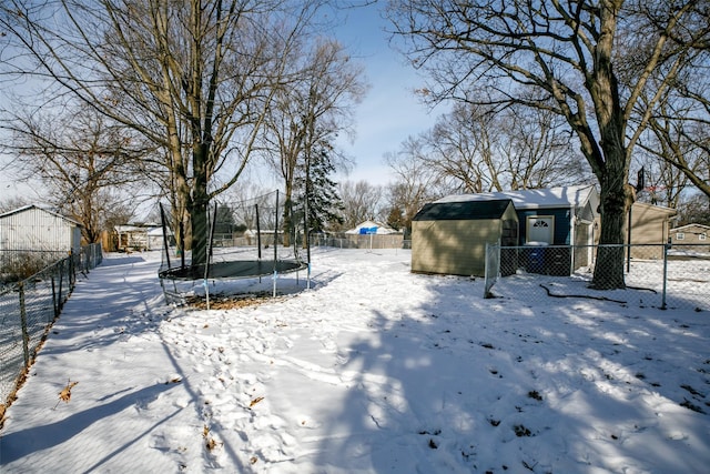 snowy yard with a trampoline, an outdoor structure, and fence