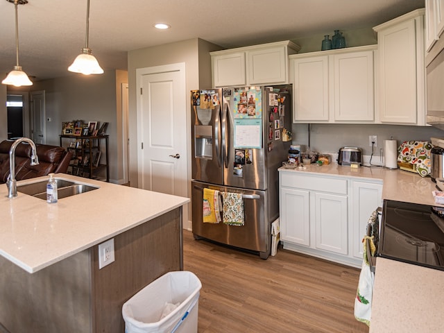 kitchen with recessed lighting, white cabinets, light wood finished floors, a sink, and stainless steel fridge